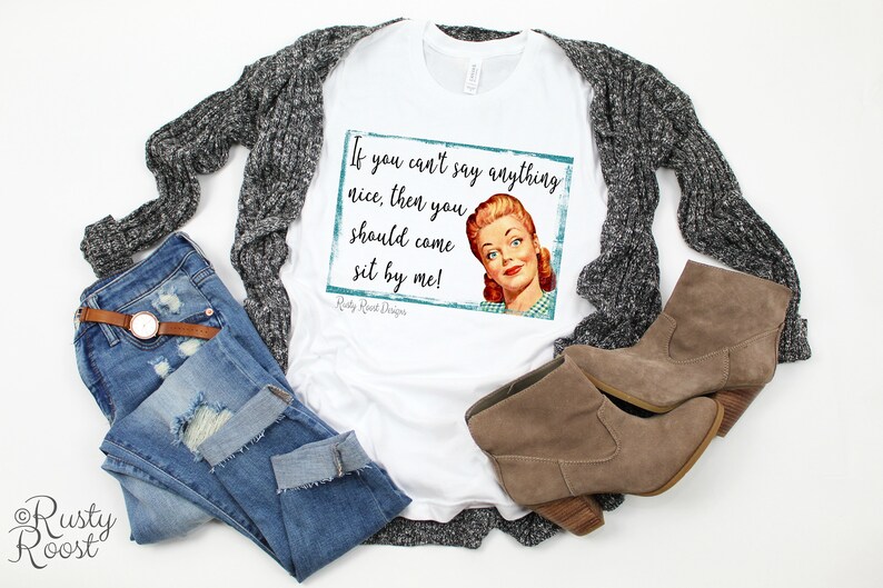 May include: White t-shirt with a vintage-style graphic featuring a woman and the text "If you can't say anything nice, then you should come sit by me!"