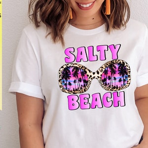 May include: White t-shirt with a pink graphic design that says "Salty Beach" with a pair of sunglasses with a leopard print frame and a palm tree design inside the lenses.