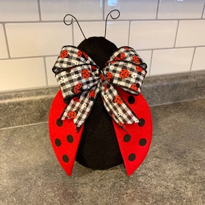 May include: A black and red ladybug doorstop with a black and white checkered bow. The bow has a ladybug print.