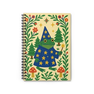 May include: Spiral-bound notebook featuring a whimsical illustration of a green frog wizard in a blue robe with yellow stars, holding a wand. The design includes fir trees, mushrooms, and floral elements on a cream background.