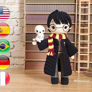 May include: Crocheted amigurumi doll of Harry Potter wearing a black robe, glasses, and a yellow and red scarf. The doll is holding a small white crocheted owl. The doll is standing in front of a bookshelf with a ladder.