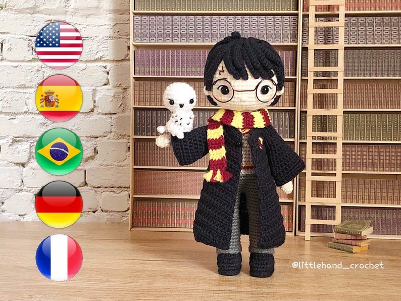 May include: Crocheted amigurumi doll of Harry Potter wearing a black robe, glasses, and a yellow and red scarf. The doll is holding a small white crocheted owl. The doll is standing in front of a bookshelf with a ladder.