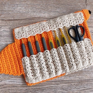 May include: A crocheted fox-shaped case with a beige interior and orange exterior. The case has eight slots for holding knitting needles and a separate slot for scissors. The case is open and the needles and scissors are visible.