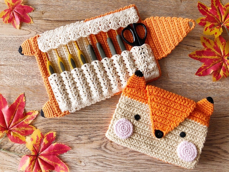May include: A crocheted fox-shaped needle case with a white interior and orange exterior. The case is open to reveal a set of crochet hooks and a pair of scissors.