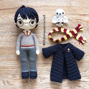 May include: Crocheted Harry Potter doll with a black robe, a red and yellow scarf, and a white owl. The doll has black hair, round glasses, and a grey sweater with a red and gold stripe.