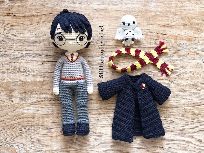 May include: Crocheted Harry Potter doll with a black robe, a red and yellow scarf, and a white owl. The doll has black hair, round glasses, and a grey sweater with a red and gold stripe.