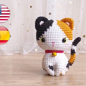May include: A crocheted calico cat toy with black, white, and orange yarn. The cat has a pink collar with a gold bell.