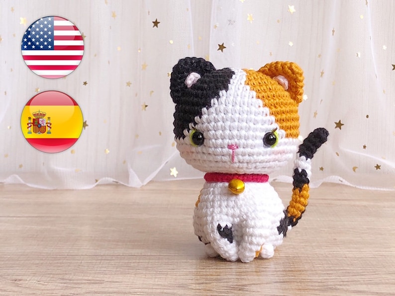 May include: A crocheted calico cat toy with black, white, and orange yarn. The cat has a pink collar with a gold bell.