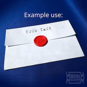 May include: White envelope with the text "YOUR TASK" stamped in black ink. A red wax seal with "TM" is affixed to the envelope. The words "Example use:" are above the envelope.