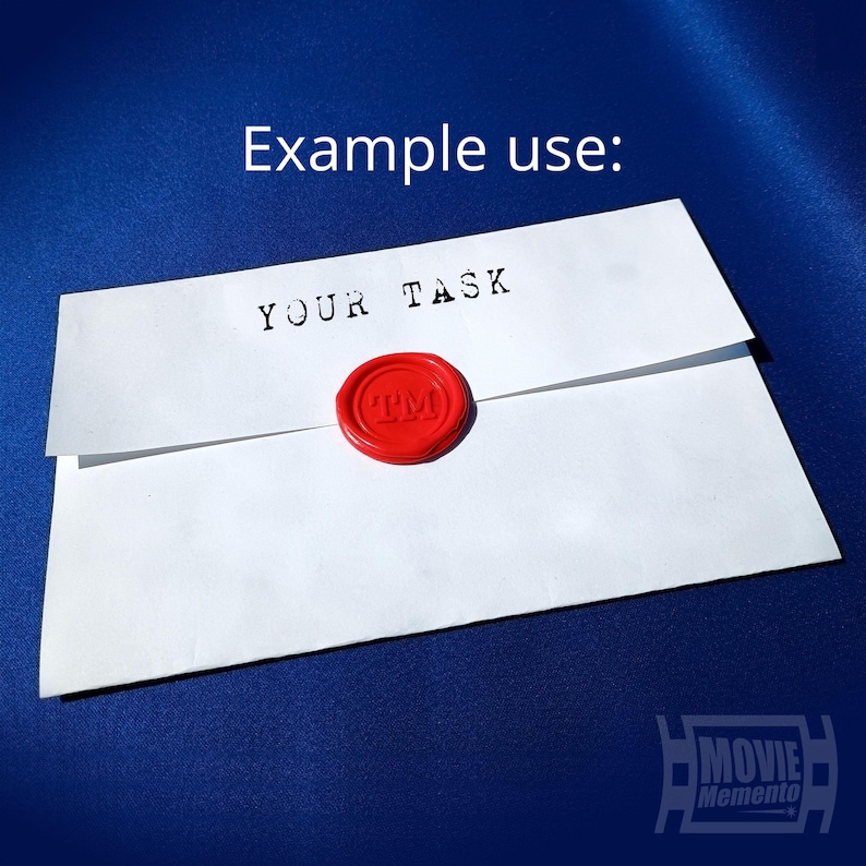 May include: White envelope with the text "YOUR TASK" stamped in black ink. A red wax seal with "TM" is affixed to the envelope. The words "Example use:" are above the envelope.