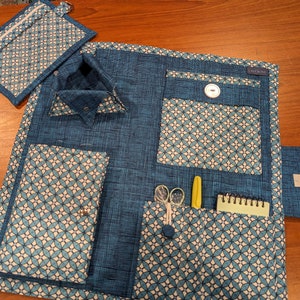 May include: A blue and white patterned sewing organizer with multiple pockets, a small notepad, scissors, and a pen. A matching zippered pouch is also included. The organizer has a button closure and a label that reads "LAKEWIND".