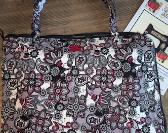 May include: A rectangular quilted tote bag featuring a repeating floral and paisley pattern in shades of black, white, grey, and deep red. The bag has two matching fabric handles, a black zipper closure, and a small rectangular red brand tag.