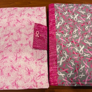 May include: Two pink and gray fabric covers with pink ribbon designs. The covers have a pocket on the front with a pink ribbon pin.