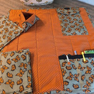 May include: A green and orange fabric organizer with multiple pockets and compartments. The fabric features a butterfly pattern. The organizer is folded open to reveal the interior.