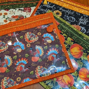 May include: Four zippered pouches with clear vinyl windows. The pouches feature different Thanksgiving-themed fabric patterns, including turkeys, pumpkins, and fall leaves. The pouches are perfect for storing small items like makeup, jewelry, or craft supplies.