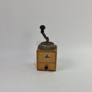 以下が含まれることがあります： 金属製の粉砕機構と引き出しが付いた、ヴィンテージの木製コーヒーグラインダー。グラインダーには、「Zassenhaus」と「Mühle」と書かれた赤と白のラベルが付いています。