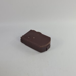 May include: A brown leather case with stitching detail. The case is closed and has a flap with a snap closure.