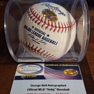 Op de afbeelding: Een witte honkbal gesigneerd door George Bell, met de inscriptie "87 M.V.P." De honkbal bevindt zich in een transparante kunststof display met een certificaat van echtheid.