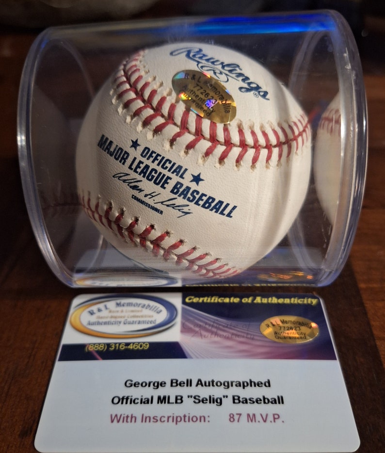 Op de afbeelding: Een witte honkbal gesigneerd door George Bell, met de inscriptie "87 M.V.P." De honkbal bevindt zich in een transparante kunststof display met een certificaat van echtheid.