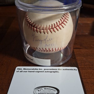 Op de afbeelding: Een witte honkbal gesigneerd door George Kell, een Hall of Fame honkballer, met de inscriptie "HOF '83". De honkbal bevindt zich in een doorzichtige plastic container met een witte kaart eronder die luidt: "R&L Memorabilia Inc. garandeert de authenticiteit van al onze handgesigneerde handtekeningen." De kaart heeft ook een rond zegel met de tekst "R&L Memorabilia Echtheidsgarantie".