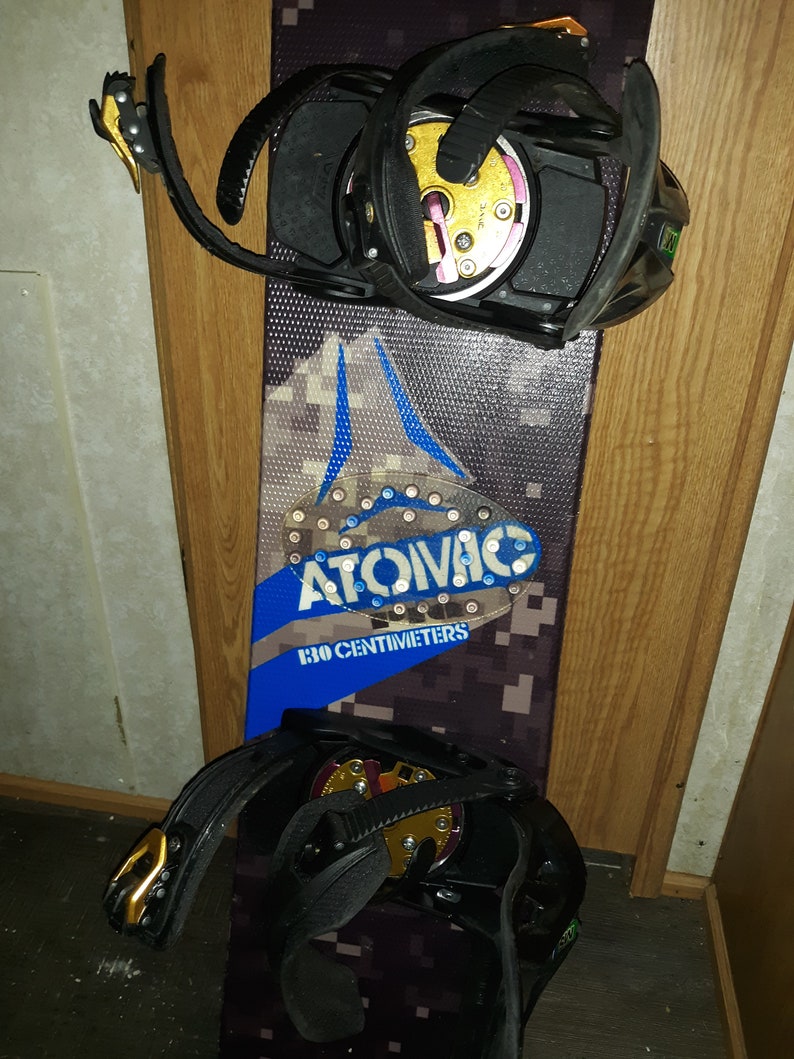 May include: A black snowboard with black and gold bindings. The snowboard has a blue and black camouflage pattern with the text "ATOIVAC 130 CENTIMETERS" printed on it.