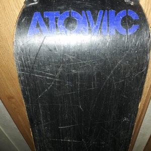 May include: Black snowboard with a blue "ATOMIC" logo on the top. The snowboard has visible scratches and wear.