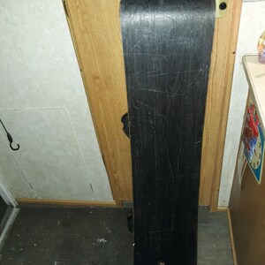 May include: A black snowboard with the word "ATOVIC" printed in blue letters on the top. The snowboard has a worn surface with scratches.