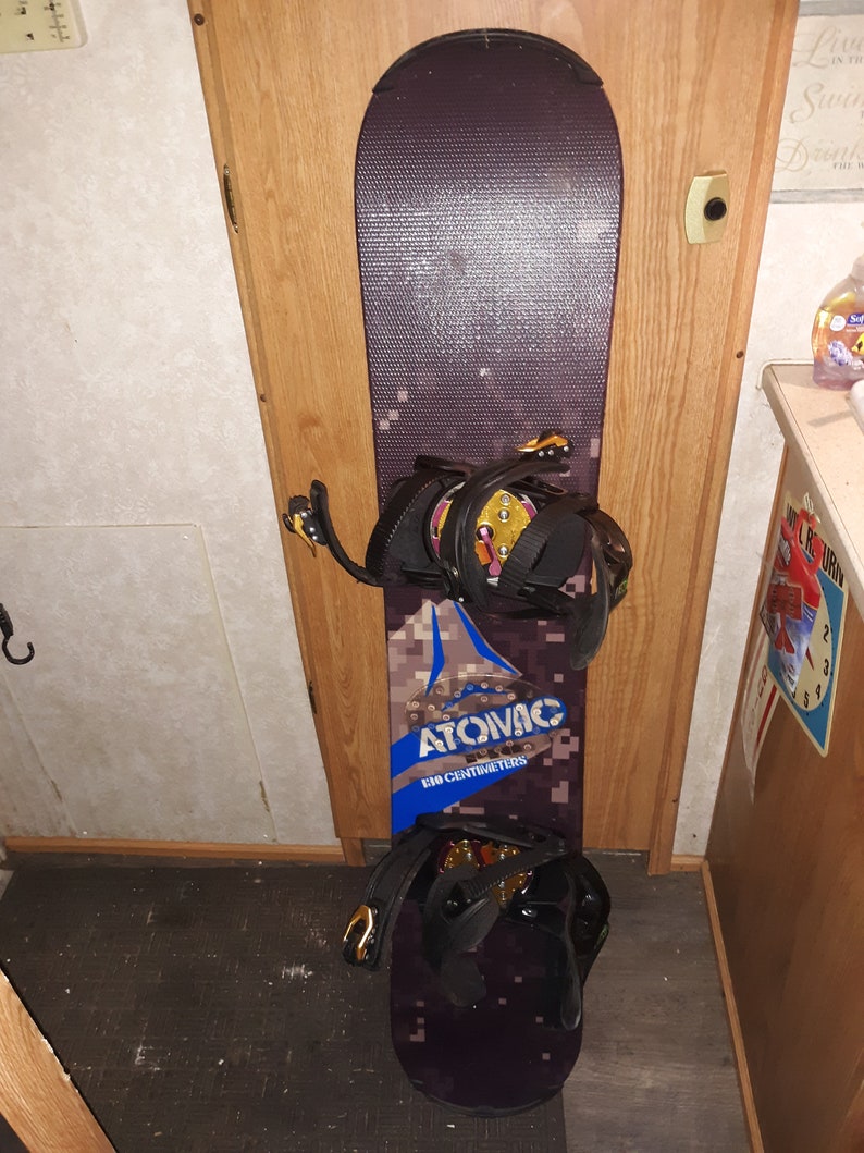 May include: A black and brown snowboard with a blue and white logo that says "Atomic 160 centimeters". The snowboard has two black bindings with gold buckles.