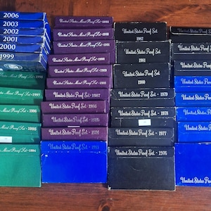 May include: A set of three ceramic canisters with lids. The canisters are white with a blue floral pattern. The largest canister is 8 inches tall, the medium is 7 inches, and the smallest is 6 inches.