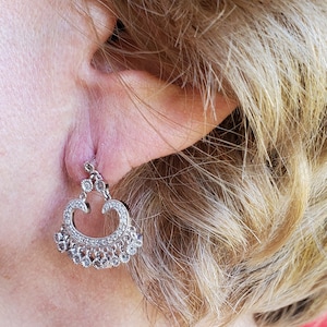 May include: A pair of silver dangle earrings with a heart-shaped design and clear stones.