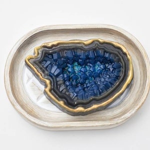 May include: A blue and gold agate geode dish with a white oval tray. The geode is a natural stone with a crystal-like texture.