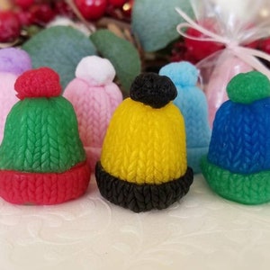 May include: Six small knitted winter hats in various colors, including pink, blue, green, yellow, and red. The hats have pom-poms on top and are arranged in a row on a white surface.