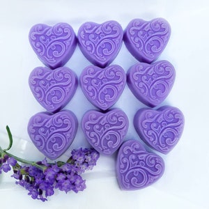 May include: Ten purple heart-shaped wax melts with a decorative swirl design. The melts are arranged in a grid pattern on a white surface.