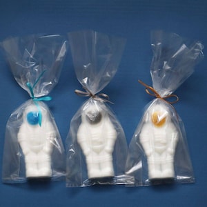 May include: Three white astronaut-shaped soaps, each with a different colored face, are individually packaged in clear plastic bags with a ribbon tie.