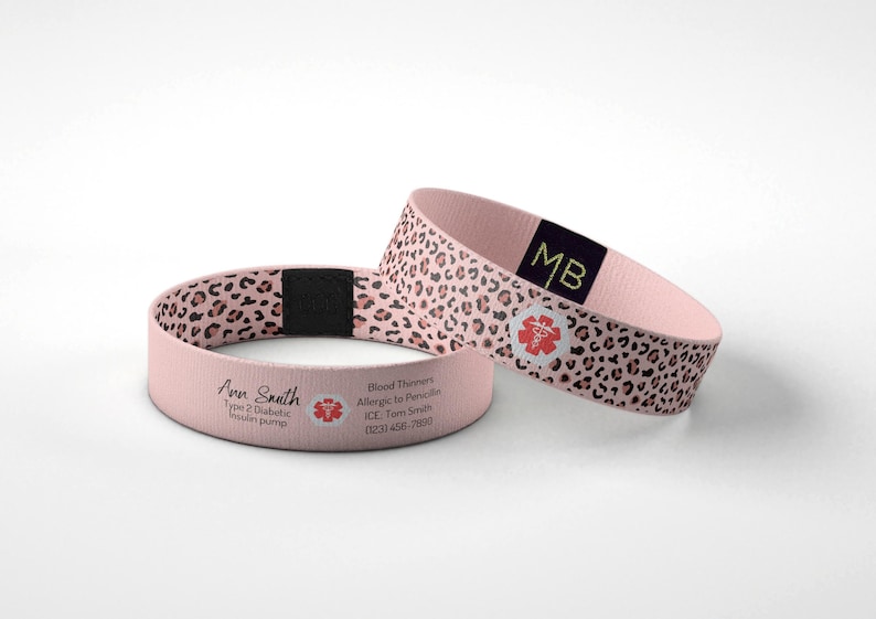 May include: Two pink medical alert bracelets. One has a leopard print design, the other has the name "Ann Smith" and medical information printed on it. Both have a red medical symbol.