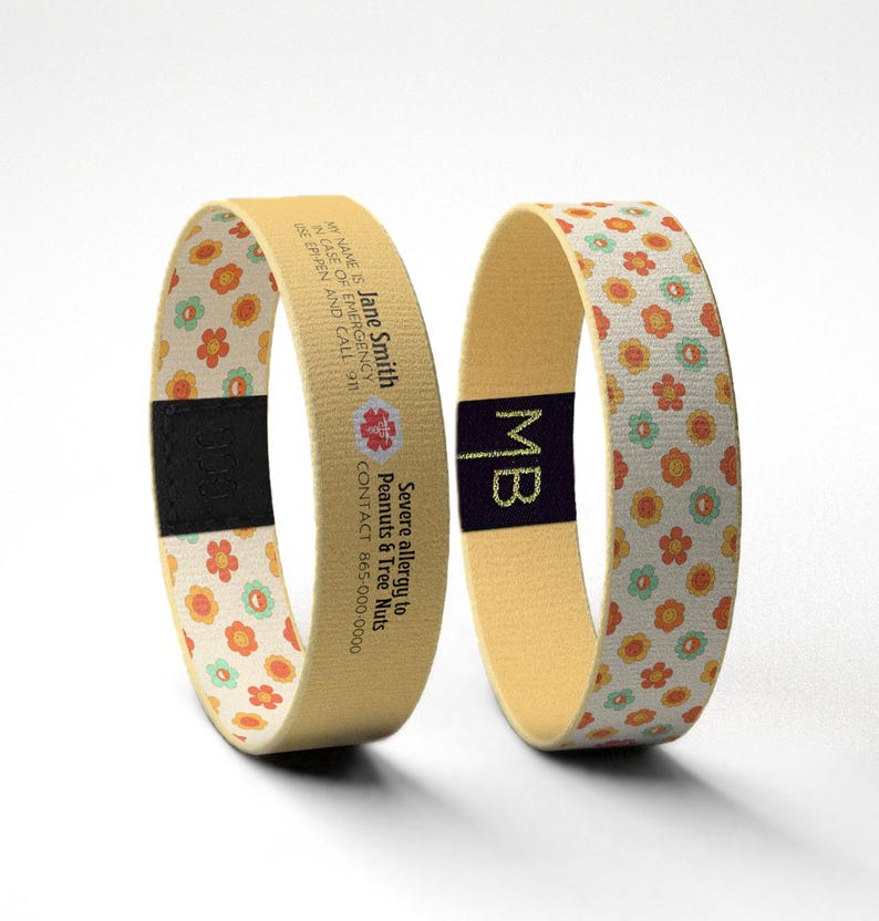 May include: Two beige medical alert bracelets. One displays the name "Jane Smith", emergency contact information, and a red medical symbol. The other has the initials "MB". Both have a floral pattern.