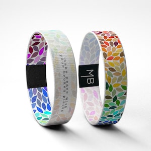 Può includere: Due braccialetti intrecciati colorati con sfondo bianco e un motivo ripetitivo di piccole foglie. Un braccialetto ha la scritta "Make peace with your broken pieces" stampata su di esso. L'altro braccialetto ha le iniziali "MB" stampate su di esso.