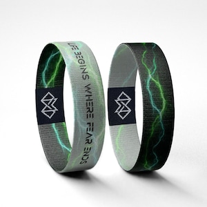 May include: Two elastic wristbands with a lightning bolt design. One band is light green with the text "LIFE BEGINS WHERE FEAR ENDS". The other band is black with green lightning. Both bands have a black label with a white geometric logo.