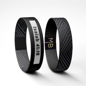 May include: Two black and gray woven wristbands. One wristband has the text "Isaiah 41:10" printed in white. The other wristband has the text "MB" printed in gold.