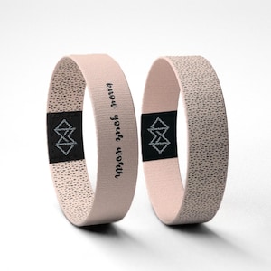Peut inclure: Deux bracelets rose clair avec un motif texturé. L'un des bracelets porte l'inscription "know your worth" en écriture noire. Les deux bracelets ont une étiquette noire avec un motif géométrique.