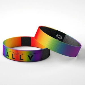 May include: Two rainbow colored wristbands with black text that reads "always an ALLY". One wristband has a black tag with the letters "MB" on it.