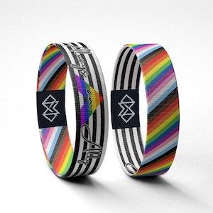 Pode incluir: Duas pulseiras de tecido com desenhos de bandeira do orgulho arco-íris. Uma pulseira tem listras brancas e pretas com o texto "Always an Ally" e um coração arco-íris. A outra pulseira tem listras brancas e pretas com um desenho de bandeira do orgulho arco-íris. Ambas as pulseiras têm uma etiqueta preta com um logotipo branco.