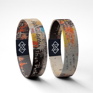May include: Two fabric bracelets with abstract art designs. One bracelet has the text "Dope is better than Perfect" and the other says "The hardest part is getting started". Each has a black label with a white geometric design.