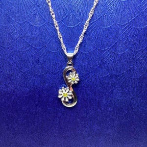 May include: A silver necklace with an infinity symbol pendant featuring two white daisies with yellow centres.