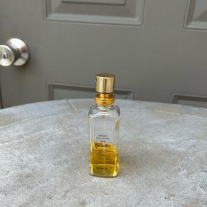 Puede incluir: Una botella de vidrio transparente de Chanel No. 5 Spray Cologne con tapa y detalles dorados. La botella es rectangular con bordes redondeados y contiene un l&iacute;quido de color dorado. La etiqueta es visible.