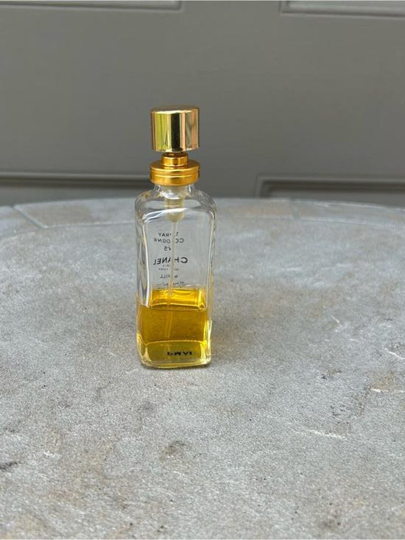 Puede incluir: Un frasco de perfume transparente y rectangular con tap&oacute;n y detalles dorados. El frasco contiene un l&iacute;quido amarillo y tiene el nombre de la marca "CHANEL" impreso. El frasco es un envase de perfume cl&aacute;sico.