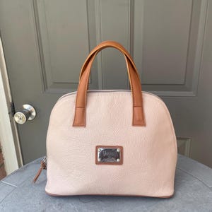 May include: A light pink leather handbag with brown leather handles and a silver metal nameplate that reads "Valentino."