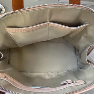 May include: The inside of a light pink leather handbag with two large pockets. The bag has a zipper closure and a silver zipper pull.
