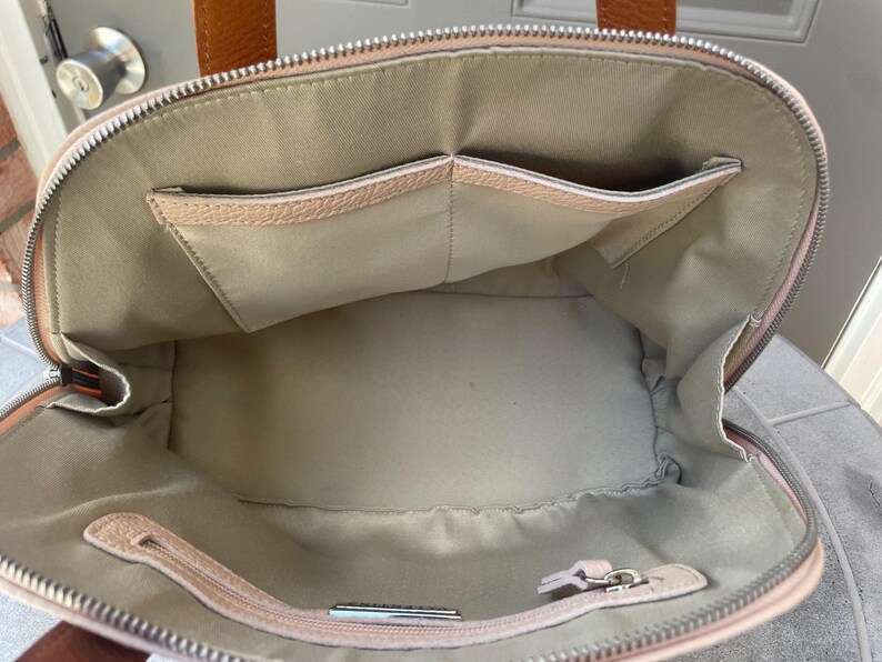 May include: The inside of a light pink leather handbag with two large pockets. The bag has a zipper closure and a silver zipper pull.