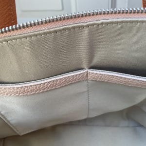 May include: The inside of a light pink handbag with a light gray fabric lining and a smaller pocket.